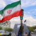 TOPSHOT - A man stands with an Iranian national flag along an intersection at Valiasr Square in Tehran on April 6, 2026. Israeli strikes killed the intelligence chief of Iran's Revolutionary Guards, as the Islamic republic on April 6 defied threats from the US President to devastate civilian infrastructure if it does not reopen the Strait of Hormuz. (Photo by ATTA KENARE / AFP via Getty Images) /